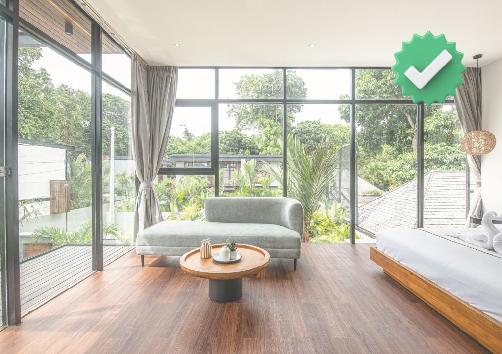 Modern luxury Bali villa bedroom with floor-to-ceiling glass windows, wooden flooring, and garden view – fully licensed villa by Short Stay Bali